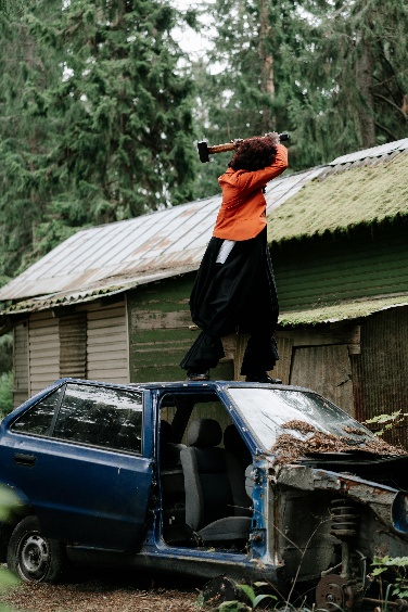 Person standing on a car in a forest, holding a hammer